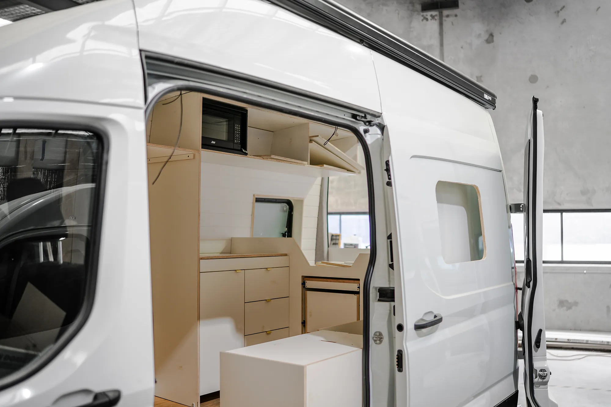 White high-roof LDV Deliver 9 campervan with sliding door open showing the CNC plywood kitchen fitout