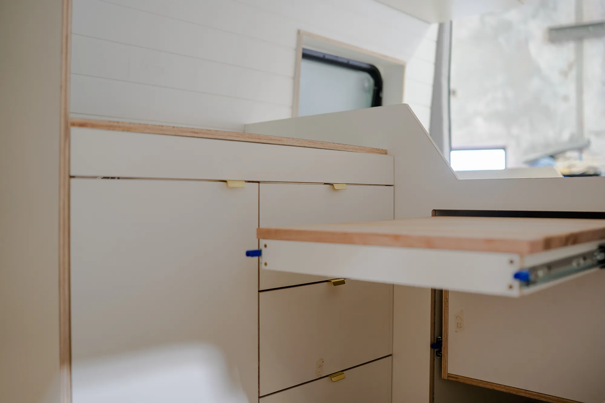 Detail of white CNC plywood kitchen drawers with brass edge pulls and the pull-out timber table extended