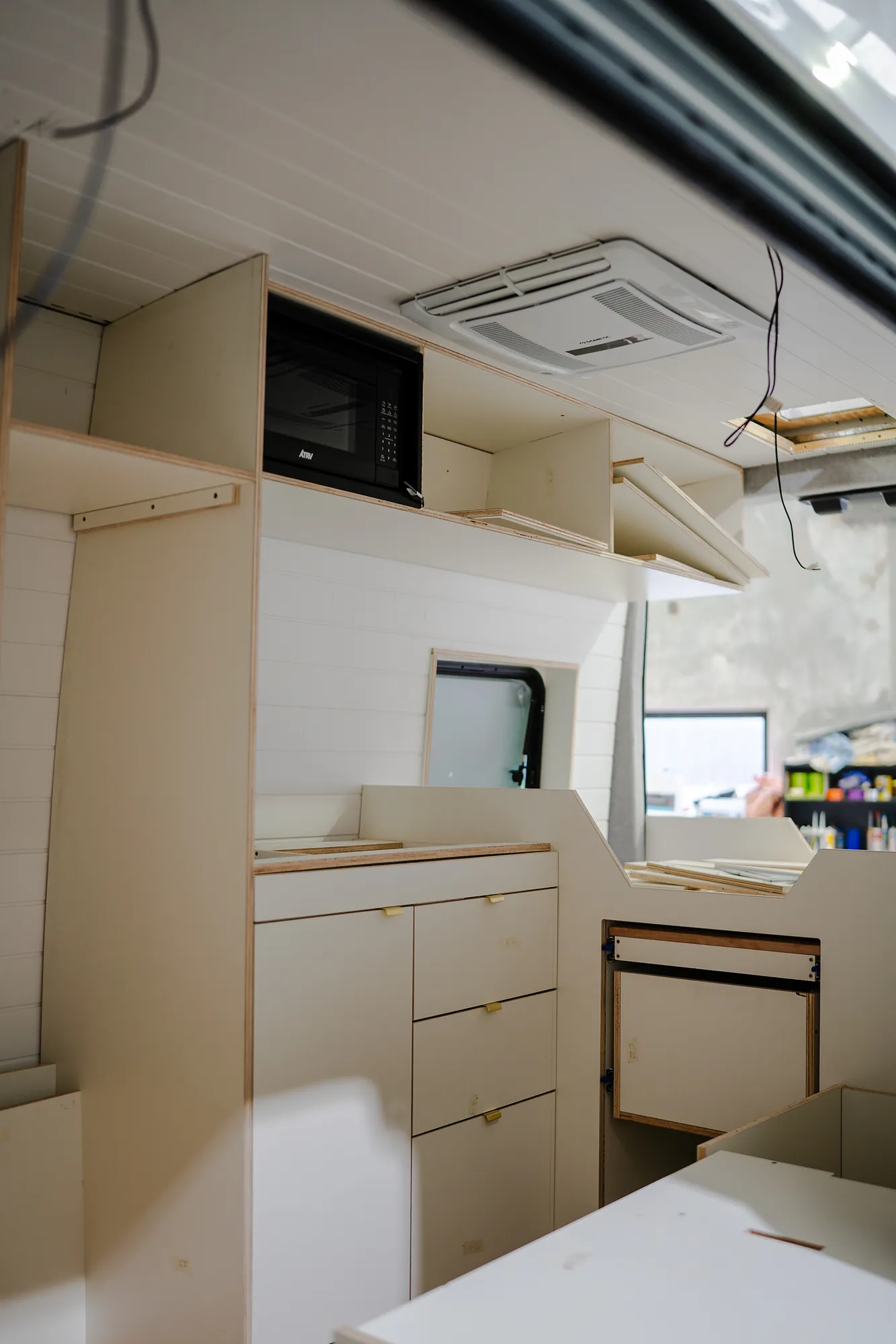 Campervan kitchen unit in white CNC plywood: drawers with brass edge pulls, overhead cabinets and pull-out table
